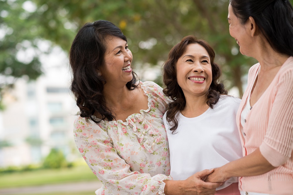 Three senior female friends laughing at chatting outdoors